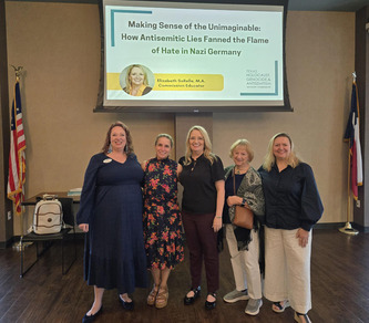 Pictured are five women smiling below a screen projector. They are in-between the Texas and US flags in the background. 