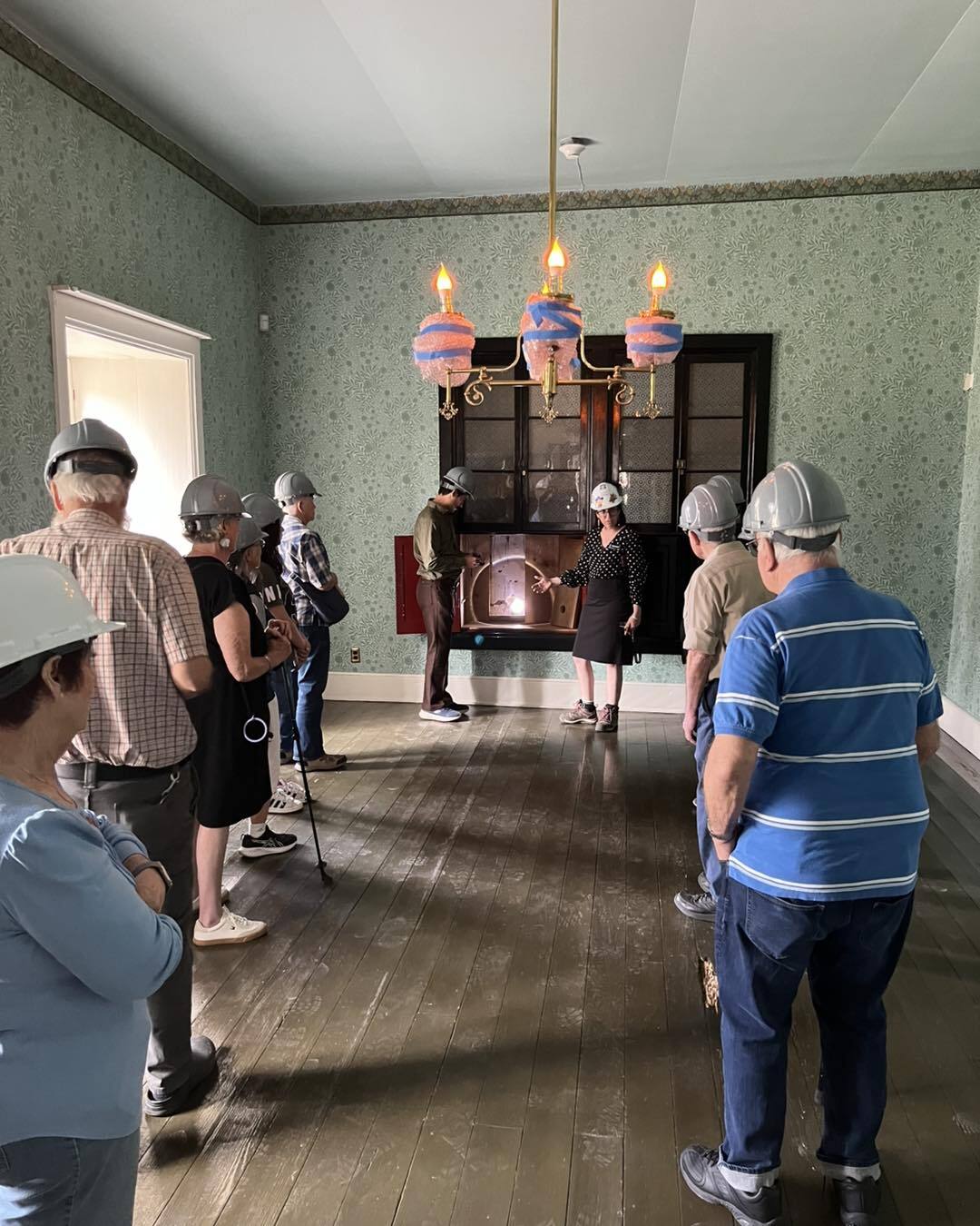 This photo shows guests touring a 19th century home while wearing hard hats.
