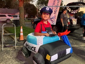 Kid dressed up as a police officer in an inflatable police car.