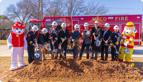 Image of City of Waco officials and Fire Department mascots in front of a fire engine at the ceremonial groundbreaking for Fire Station 15.
