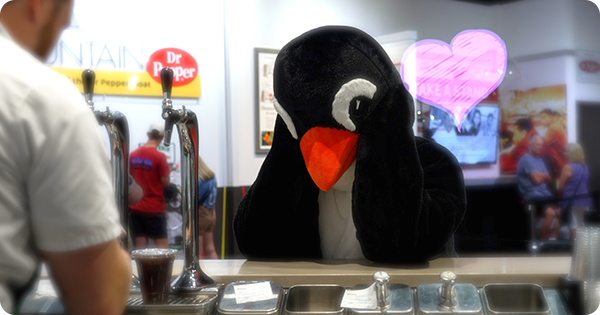 Person in a penguin costume behind a counter watching a Dr Pepper Museum employee prepare soda in adoration