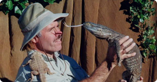 Man holding a reptile up to his face while a smaller reptile sits on his shoulder