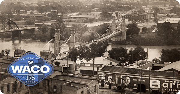 Black and white photo of the Suspension Bridge with a train crossing parallel to the Brazos River.