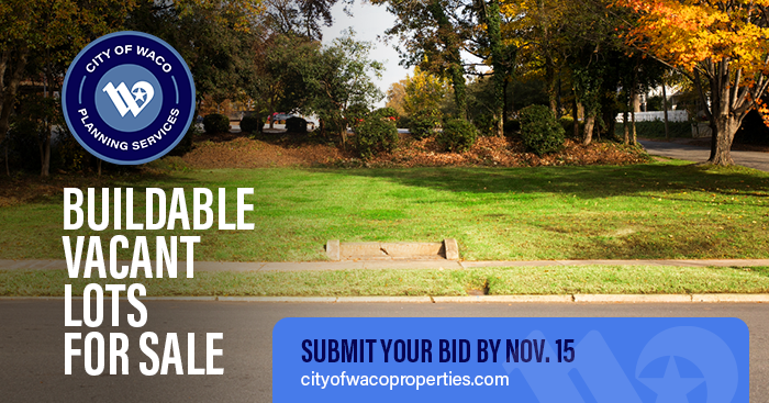 An empty lot with a sidewalk and fall foliage in the background