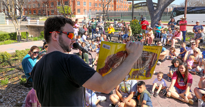 A man reading a book to children outside