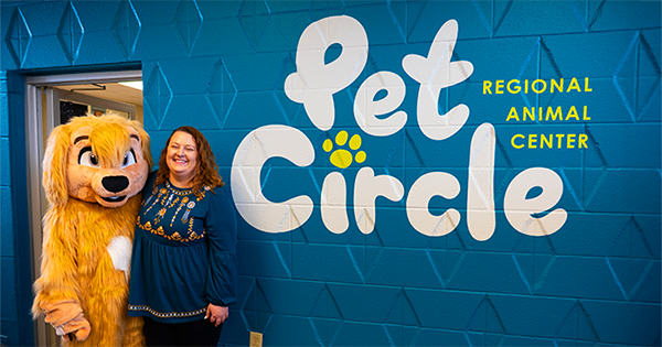 Melissa Sheldon with Chance the dog mascot in front of Pet Circle mural
