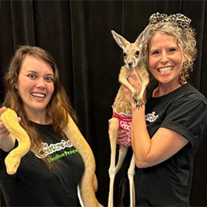 Two women, one holding a yellow snake, the other holding a baby kangaroo