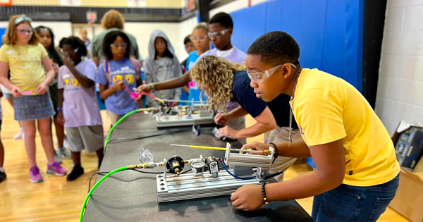 A boy wearing goggles using air pressure and mechanical equipment at a table