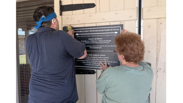 Two employees hang new signs on front doors