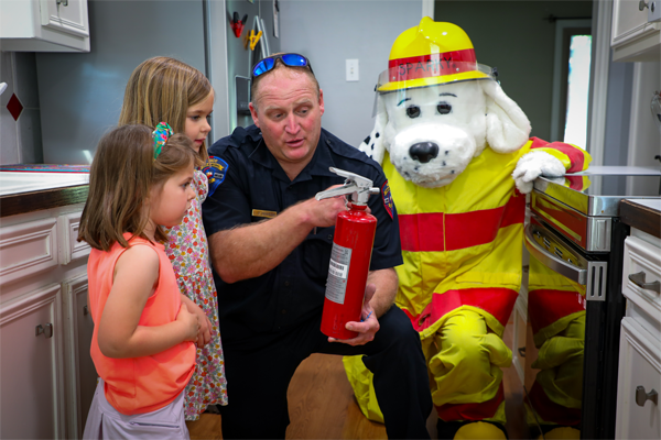 A firefighter and Sparky the Fire Dog showing two girls how to use a fire extinguisher