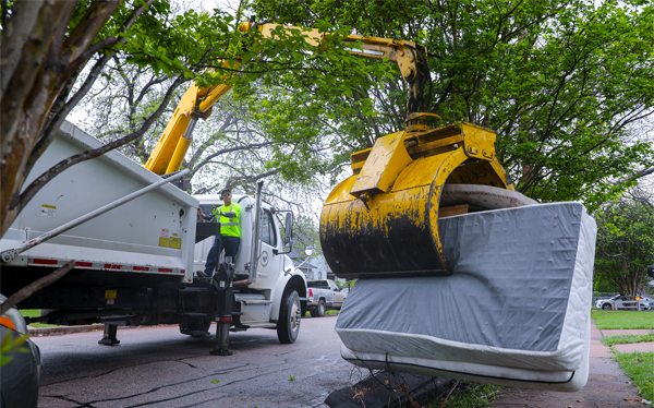 Man operating a crane from a solid waste truck picking up a mattress