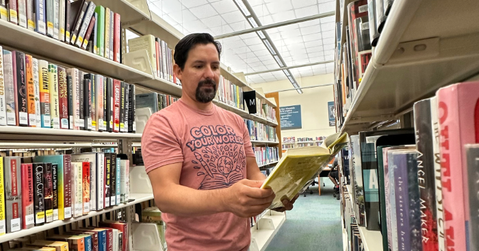 A man reading a book in a library aisle