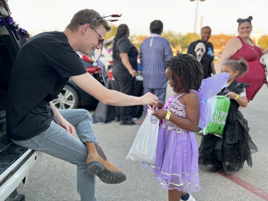 man giving a child candy at a trunk or treat event