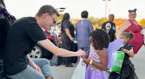 A man handing out candy to a kid at a trunk or treat event