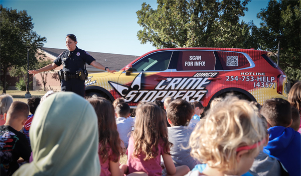 Female Waco Police officer talking to kids in front of Crime Stoppers car