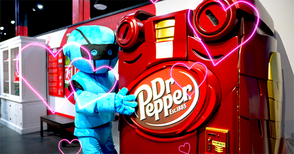 Blue robot mascot hugging a Dr Pepper soda machine