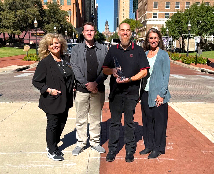 City of Waco staff (two men and two women) holding an award in downtown Fort Worth