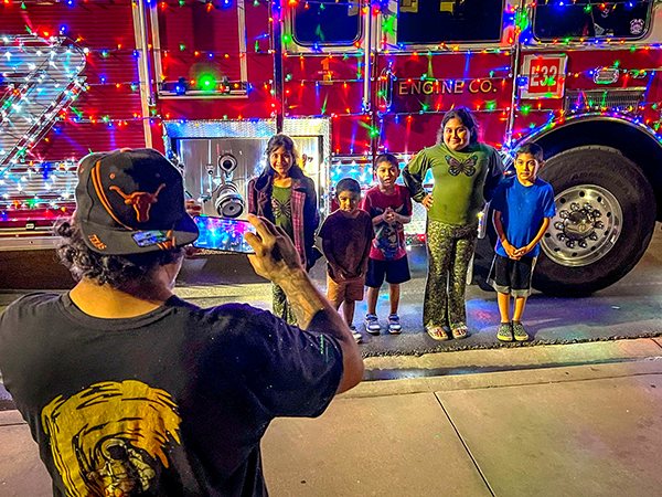 A dad taking a picture of his kids with the Holiday Fire Engine decorated in lights