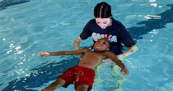 A young woman teaching a kid how to float in a pool