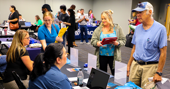 A young woman and an older man speaking to women at a booth at a job fair