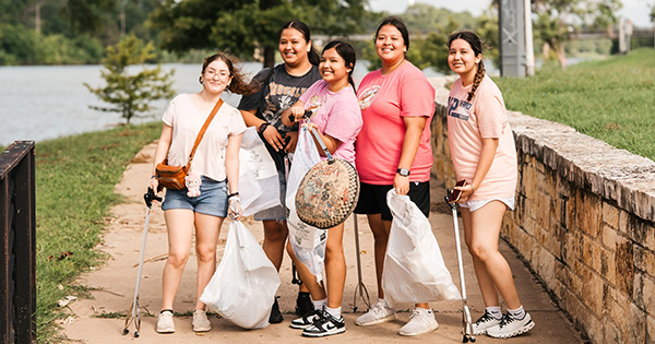 Five young women holding trash bags and trash grabbers