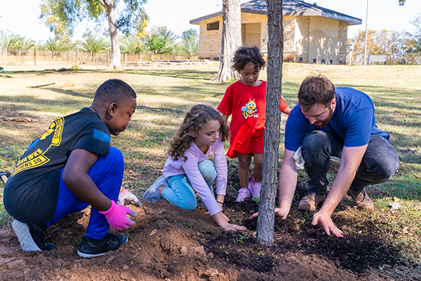Three kids planting a tree with an adult