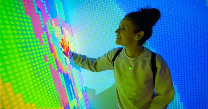 Young woman interacting with bright colored immersive and interactive wall 
