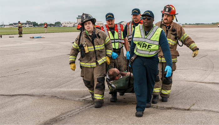 Group of firefighters dragging volunteer actor playing a disaster survivor