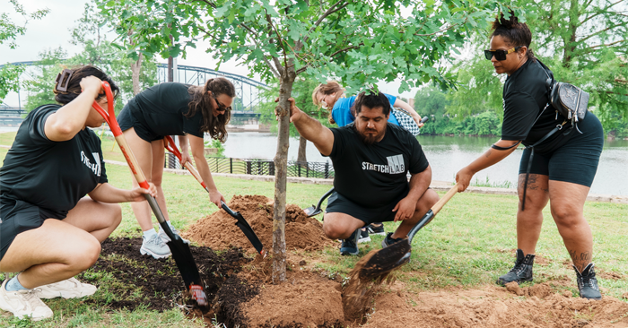Young men and women planting a tree near the riverbank