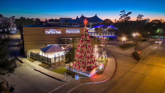 A drone image of The Ice Rink building and Christmas Tree with red and green lights at dusk.