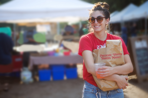 A young woman in jeans and a red shirt carries a bag of goodies at the outdoor Creekside Winter Makers Market