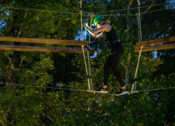 A woman in black fitness gear and a headlamp navigates a ropes course at night in The Woodlands 