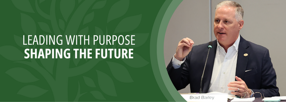 Leading with Purpose and Shaping The Future; Photo of a man in a blue suit speaking on a microphone 