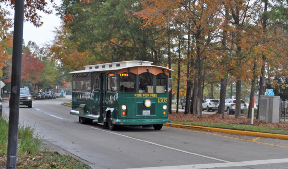 Image of a green and white trolley driving on a tree lined road