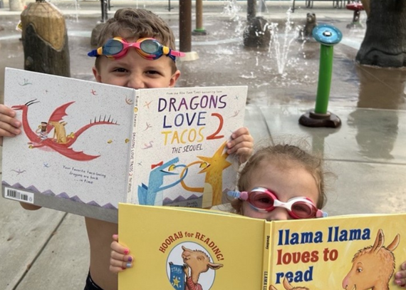 Two young children wearing swim goggles holding books at a splashpad