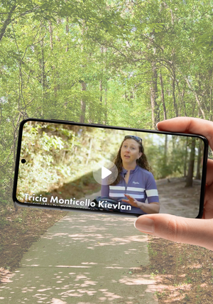 A wooded pathway background behind a cell phone displaying a video