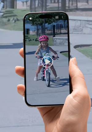  a hand holding a cell phone with an image of a young child riding a bike wearing a pink helmet