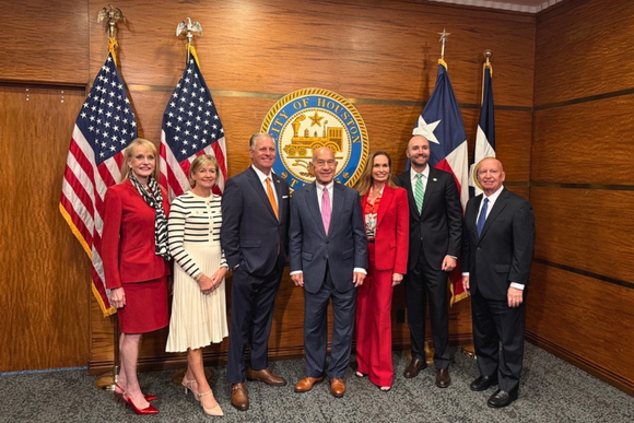Eight smiling people standing in front of the U.S flag, the Texas flag and the City of Houston Seal