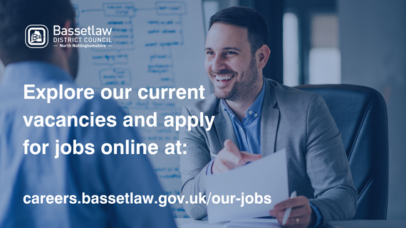 Smiling pan with a document in his hand, talking to another person across the desk.