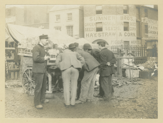 Black & white photo showing a market trader selling caged birds with customers at Saturday Rag Fair, Open Market, Moat Row, Birmingham in 1897.