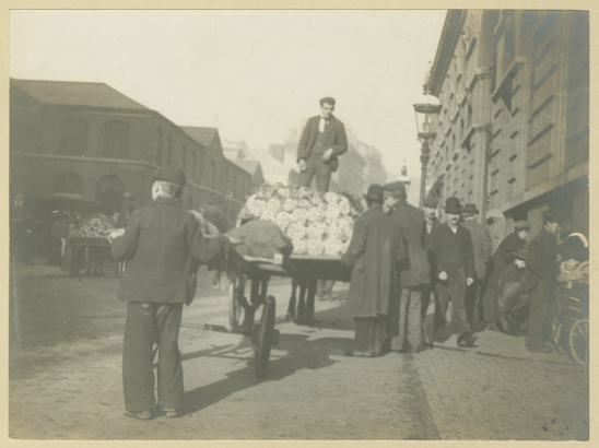 Black & white photo of a street scene showing people & hand-carts at the Vegetable &Fruit Market, Jamaica Row, Birmingham in 1899.