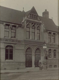 Sepia photo showing the ornate terracotta Constitution Hill Library building. A man stand outside the front next to a lamppost.