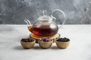 Glass teapot full of tea and three wooden bowls with loose leaf tea