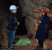 Two women wearing helmets and head torches standing talking in a cave