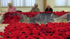 Women sewing poppies onto a large net