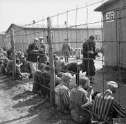 Prisoners sitting by the wire fence, eating their first meal after the liberation of Bergen-Belsen Concentration Camp, © IWM BU 4006