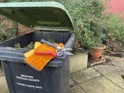 Green-lidded bin with gardening tools on lid