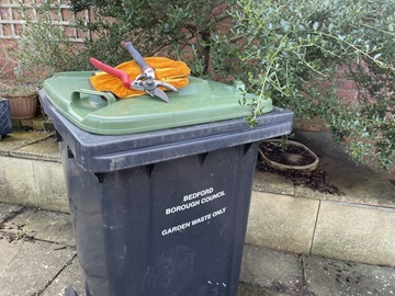 Green-lidded wheelie bin with gardening tools on lid