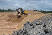 A yellow digger sits with its arm raised within a sand mining quarry. The sand is a mid-brown colour.