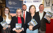  Members of GSNI stand together holding copies of the book. Behind them are banners for the British Geological Survey &  GSNI